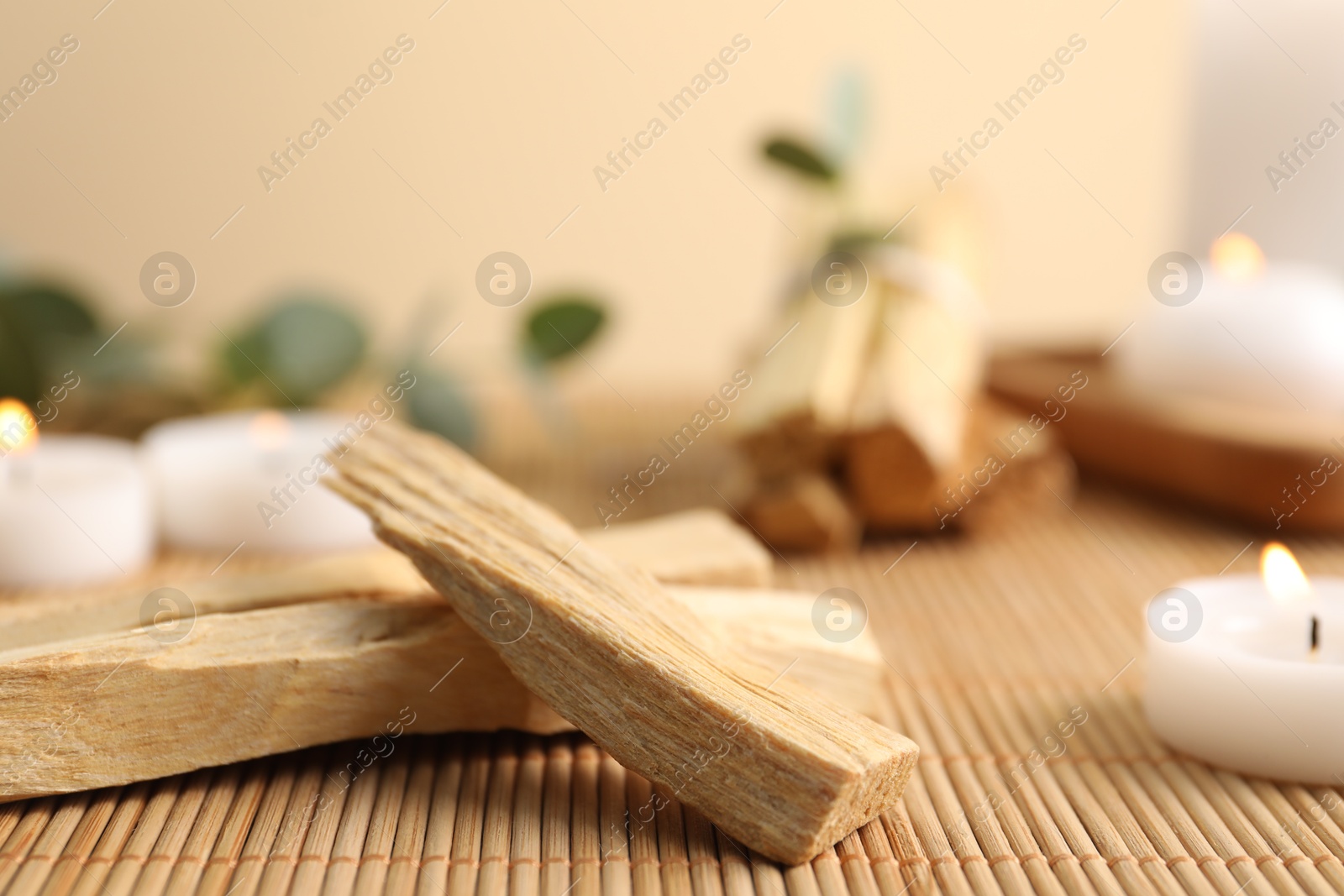 Photo of Palo santo sticks and burning candles on bamboo mat, closeup