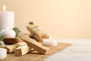 Photo of Palo santo sticks and burning candles on light wooden table, closeup. Space for text