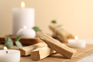 Photo of Palo santo sticks and burning candles on bamboo mat, closeup