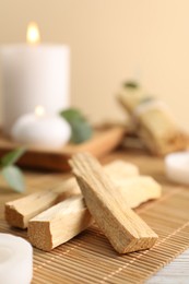 Photo of Palo santo sticks and burning candles on bamboo mat, closeup