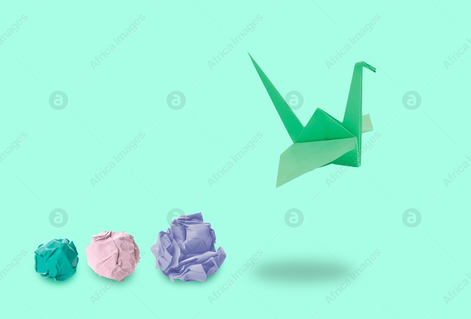 Image of Green origami crane and crumpled paper balls on aquamarine color background. Transformation or new ideas concept