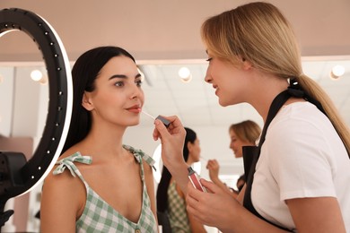 Photo of Professional makeup artist working with beautiful young woman in salon. Using ring lamp