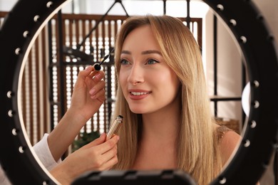 Photo of Professional makeup artist applying mascara onto woman's eyelashes in salon, view through ring lamp