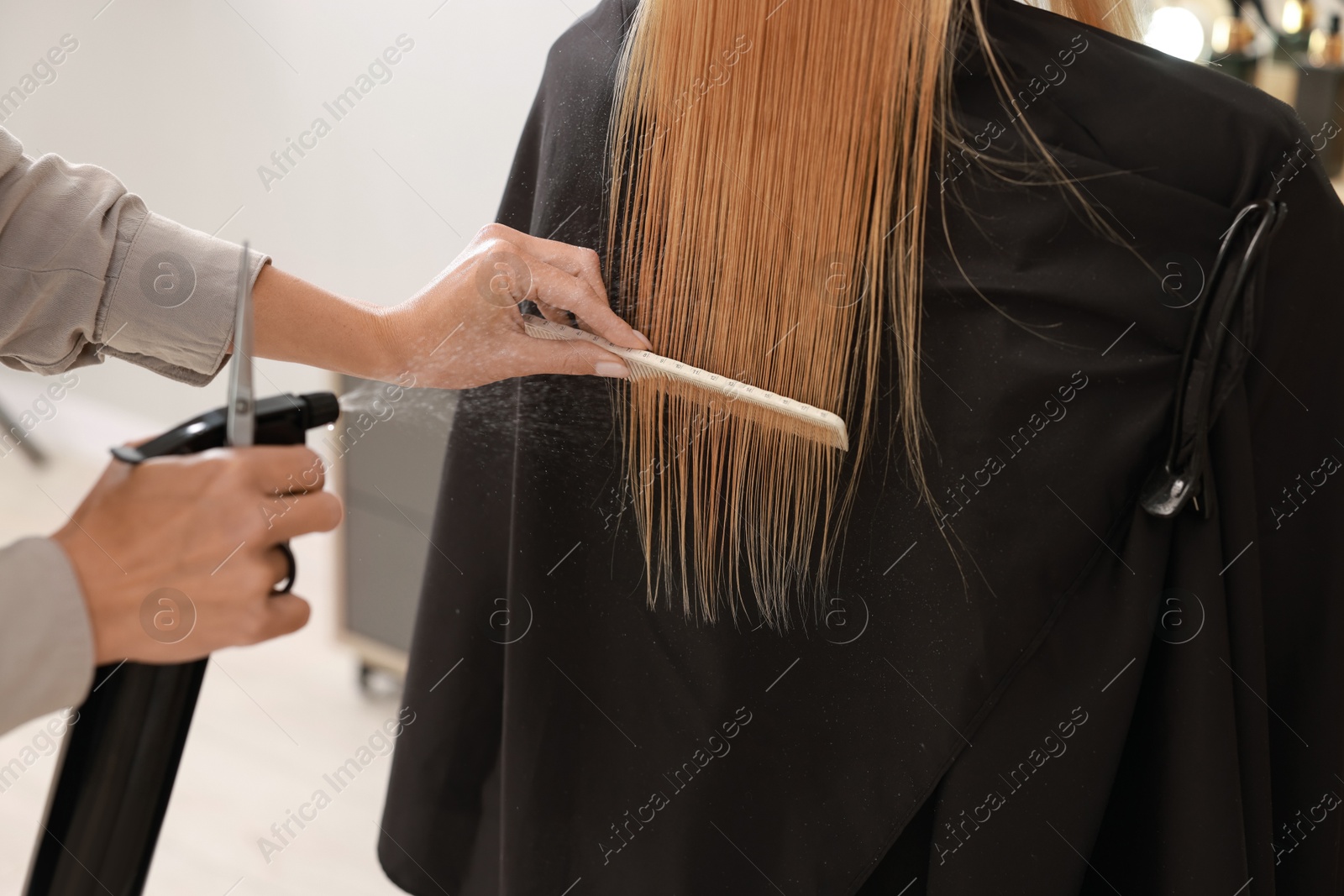 Photo of Hairdresser using spray while making stylish haircut in salon, closeup