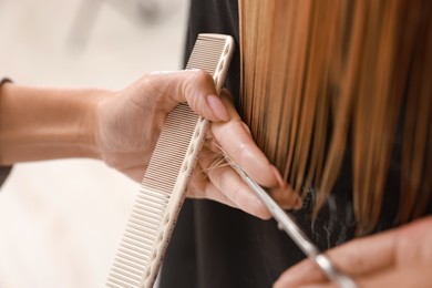 Photo of Hairdresser cutting client's hair with scissors in salon, closeup