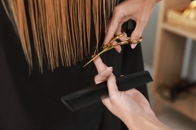 Photo of Hairdresser cutting client's hair with scissors in salon, closeup