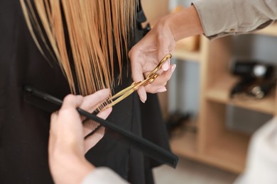 Photo of Hairdresser cutting client's hair with scissors in salon, closeup