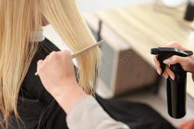 Photo of Hairdresser using spray while making stylish haircut in salon, closeup