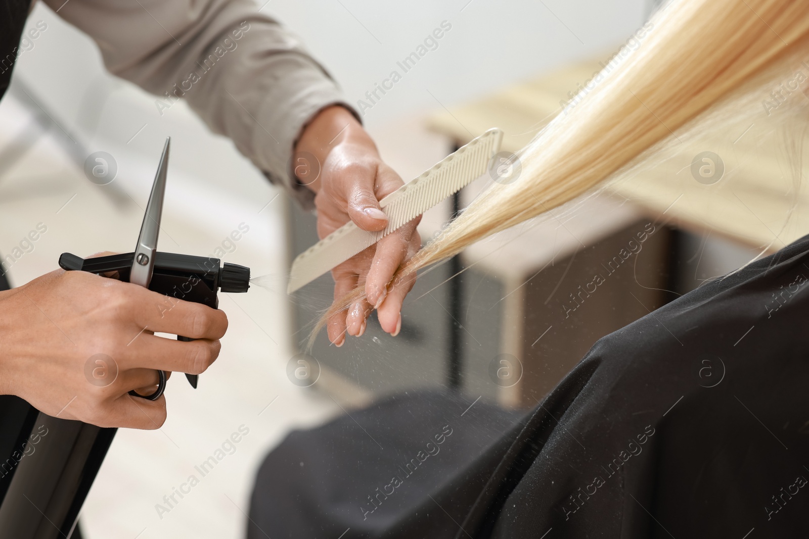 Photo of Hairdresser using spray while making stylish haircut in salon, closeup