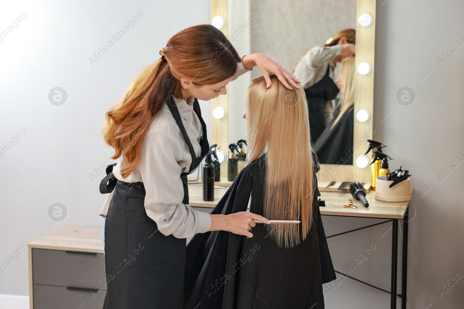 Photo of Professional hairdresser combing woman's hair in salon