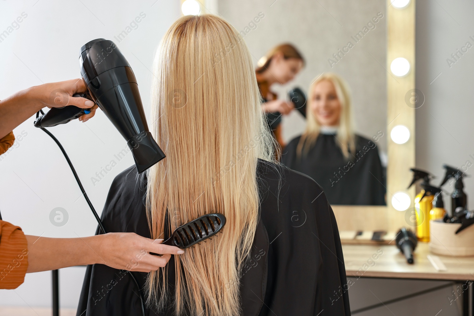 Photo of Hairdresser blow drying client's hair in salon, closeup