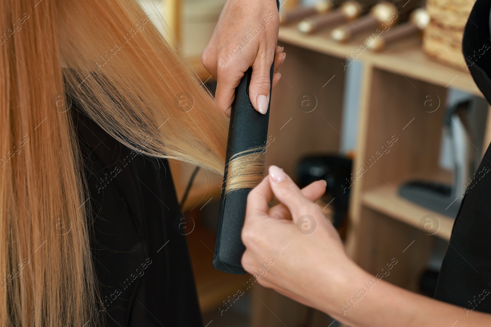 Photo of Hairdresser curling woman's hair with flat iron in salon, closeup