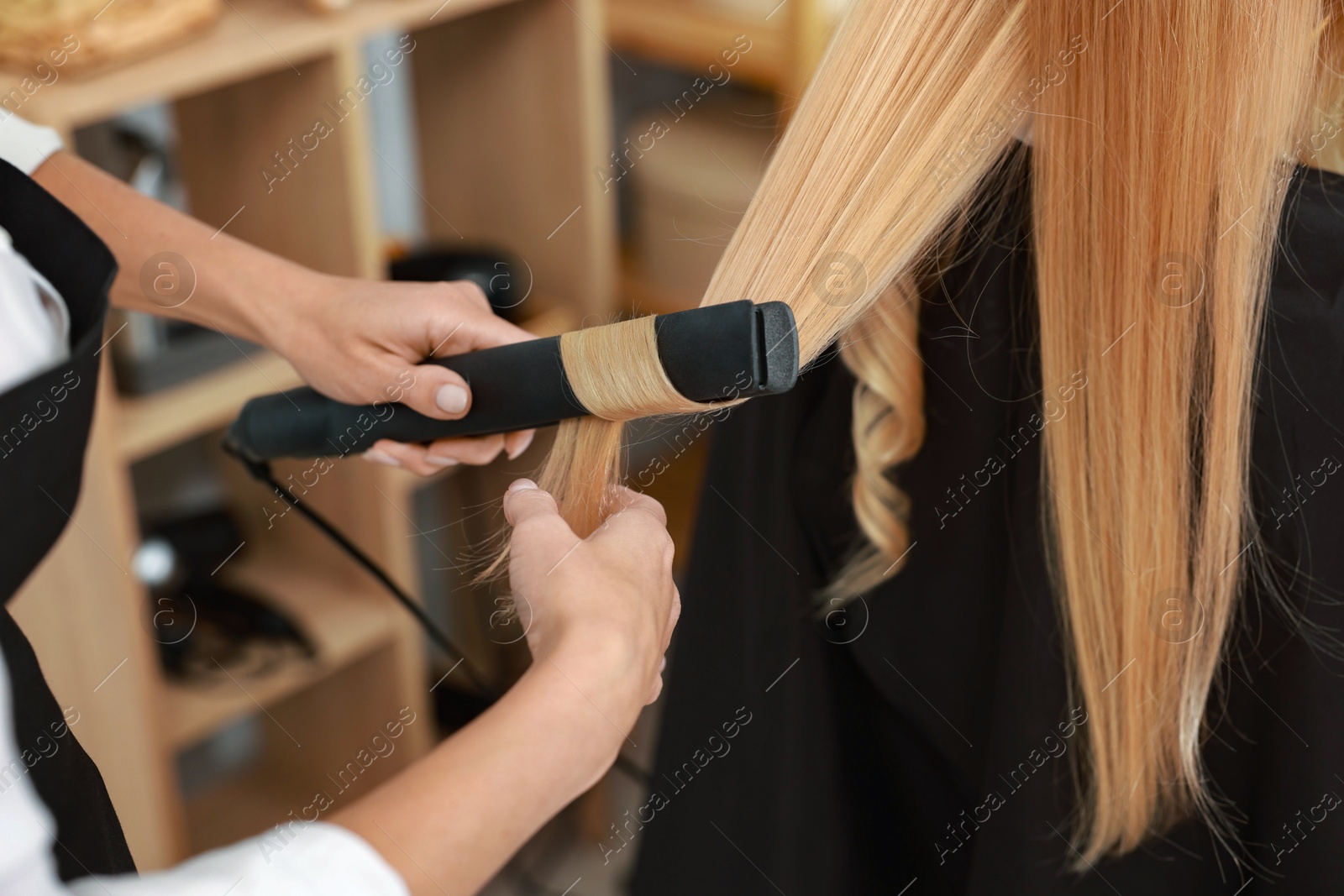 Photo of Hairdresser curling woman's hair with flat iron in salon, closeup