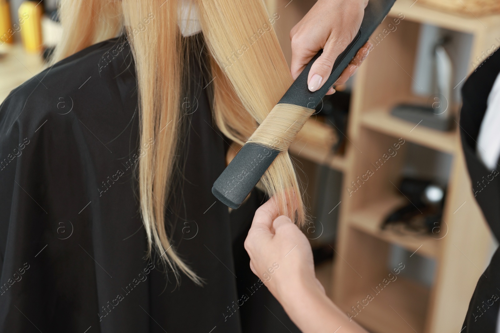 Photo of Hairdresser curling woman's hair with flat iron in salon, closeup