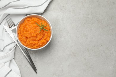 Photo of Tasty mashed sweet potato with rosemary in bowl served on grey textured table, flat lay. Space for text