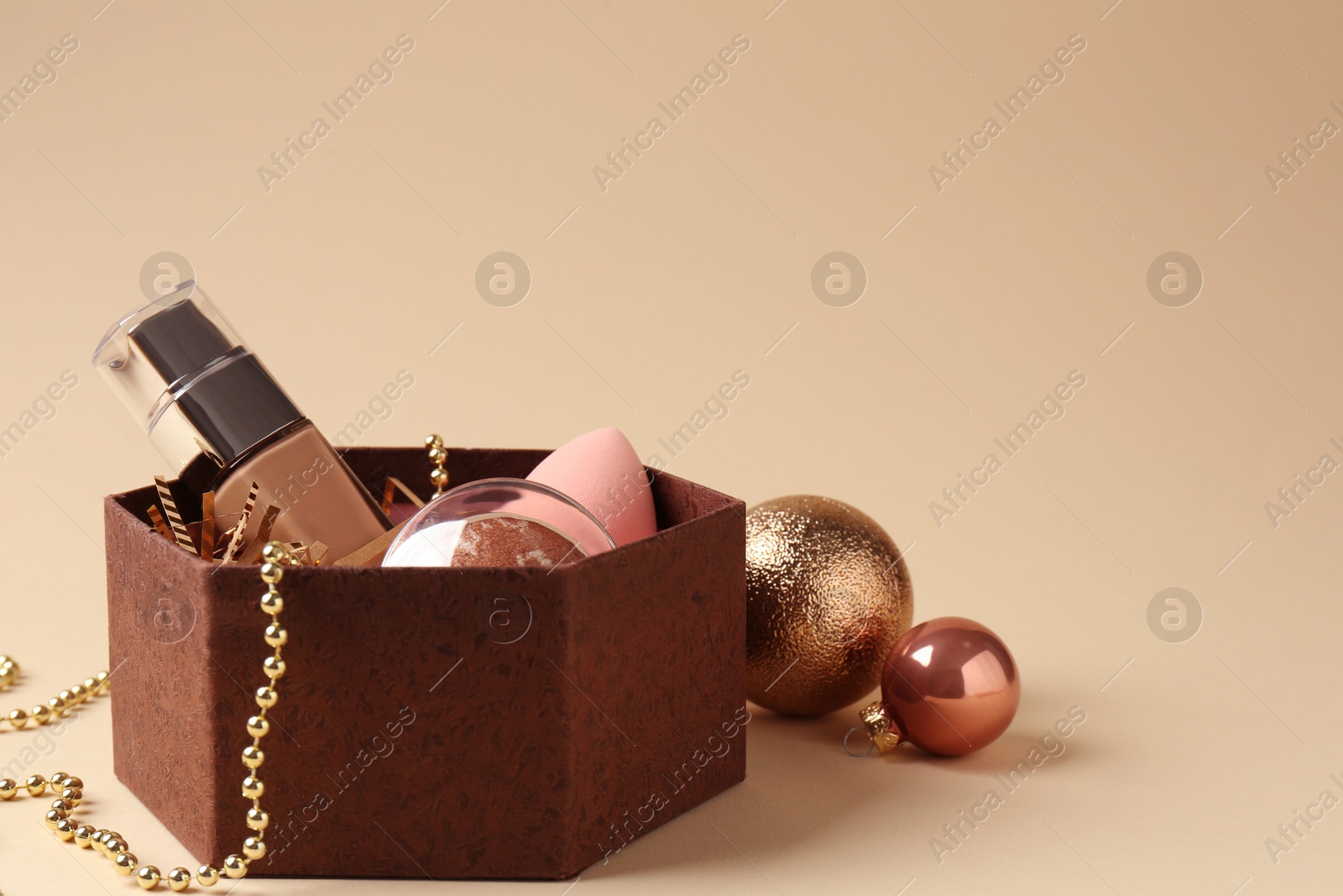 Photo of Cosmetic products in gift box and Christmas balls on beige background, space for text