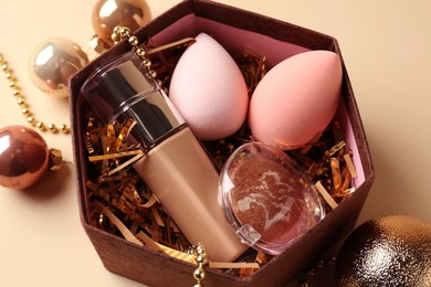 Photo of Cosmetic products in gift box and Christmas balls on beige background, closeup