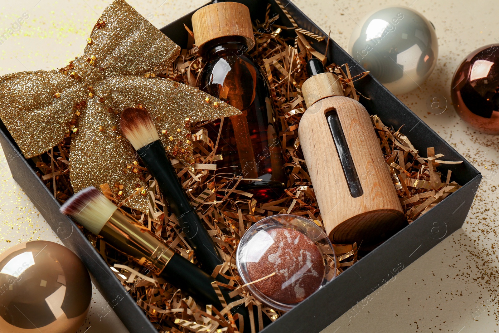 Photo of Christmas gift box with cosmetic products and festive balls on beige background, closeup