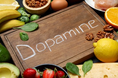 Photo of Wooden board with word Dopamine and different fresh products on grey table