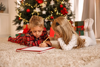 Photo of Little kids writing letter to Santa Claus on floor at home. Christmas celebration