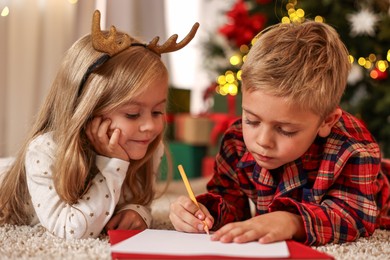 Photo of Little kids writing letter to Santa Claus on floor at home. Christmas celebration