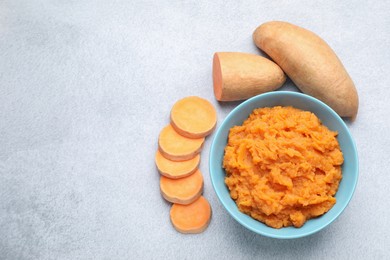 Photo of Tasty mashed sweet potato in bowl and fresh vegetables on gray table, flat lay. Space for text