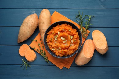 Photo of Tasty mashed sweet potato with pumpkin seeds in bowl, fresh vegetables, rosemary and thyme on blue wooden table, flat lay