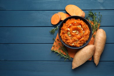Photo of Tasty mashed sweet potato with pumpkin seeds in bowl, fresh vegetables, rosemary and thyme on blue wooden table, flat lay. Space for text