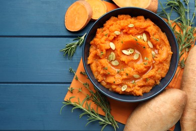 Photo of Tasty mashed sweet potato with pumpkin seeds in bowl, fresh vegetables, rosemary and thyme on blue wooden table, flat lay. Space for text