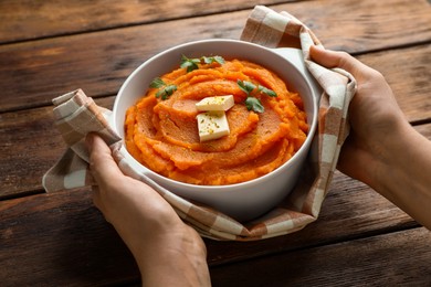 Photo of Woman with bowl of tasty mashed sweet potato at wooden table, closeup