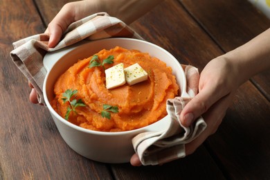Photo of Woman with bowl of tasty mashed sweet potato at wooden table, closeup