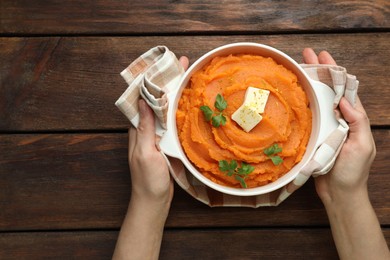 Photo of Woman with bowl of tasty mashed sweet potato at wooden table, top view