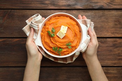 Photo of Woman with bowl of tasty mashed sweet potato at wooden table, top view