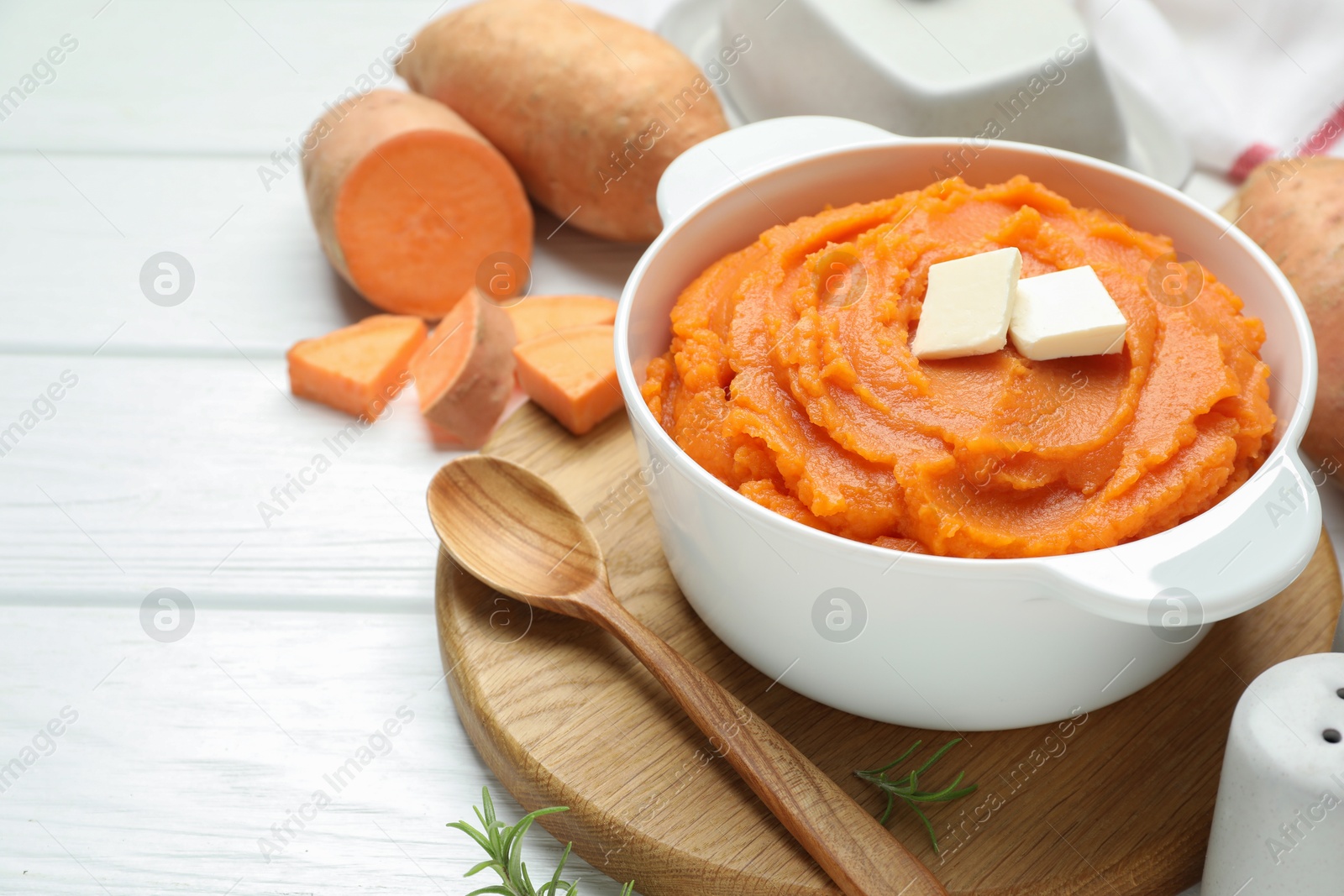Tasty mashed sweet potato with butter in bowl, spoon and fresh vegetables on white wooden table, closeup Photo of Tasty mashed sweet potato with butter in bowl, spoon and fresh vegetables on white wooden table, closeup