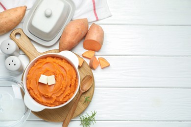Photo of Tasty mashed sweet potato with butter in bowl and fresh vegetables on white wooden table, flat lay. Space for text