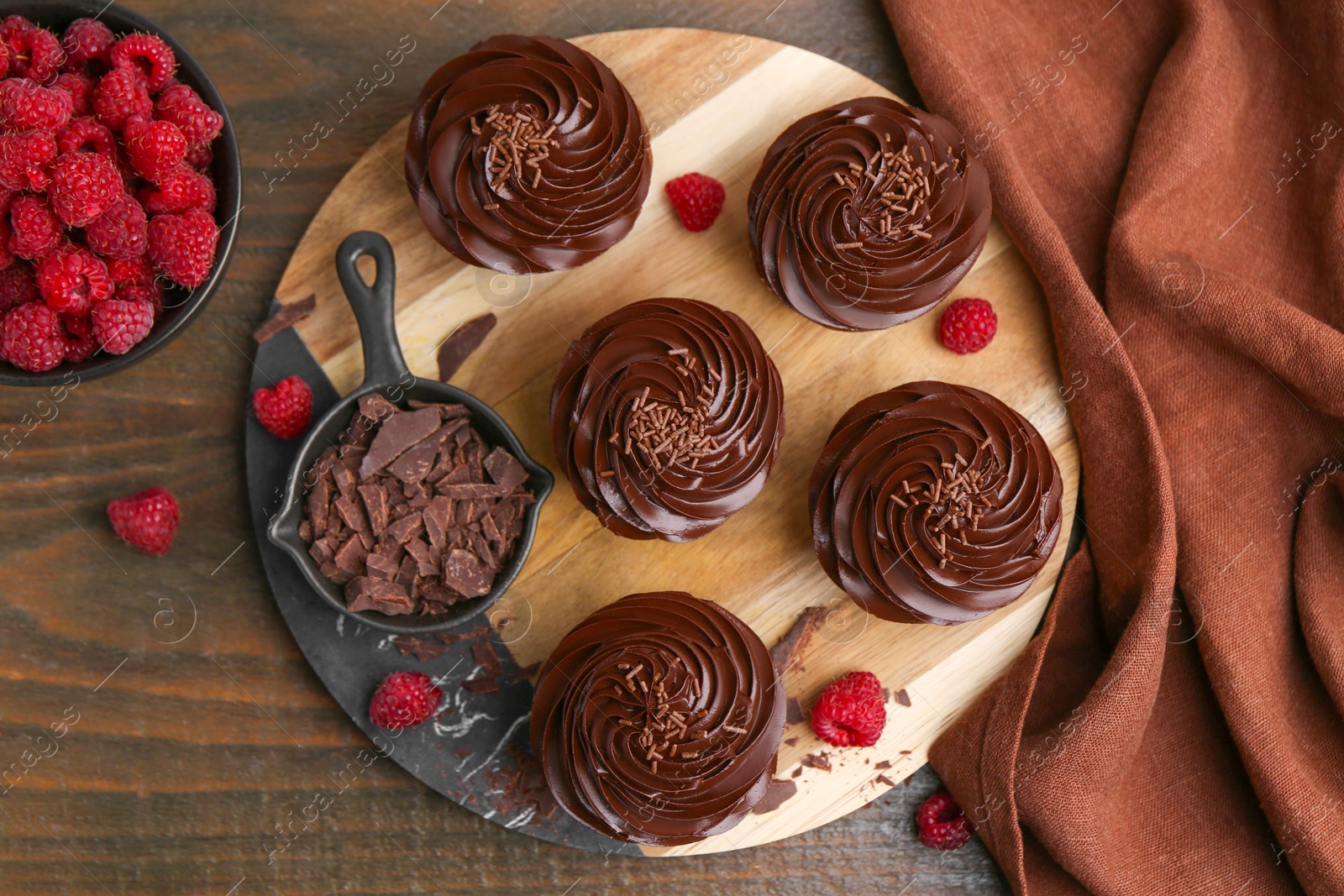 Photo of Tasty cupcakes with chocolate cream and raspberries on wooden table, flat lay