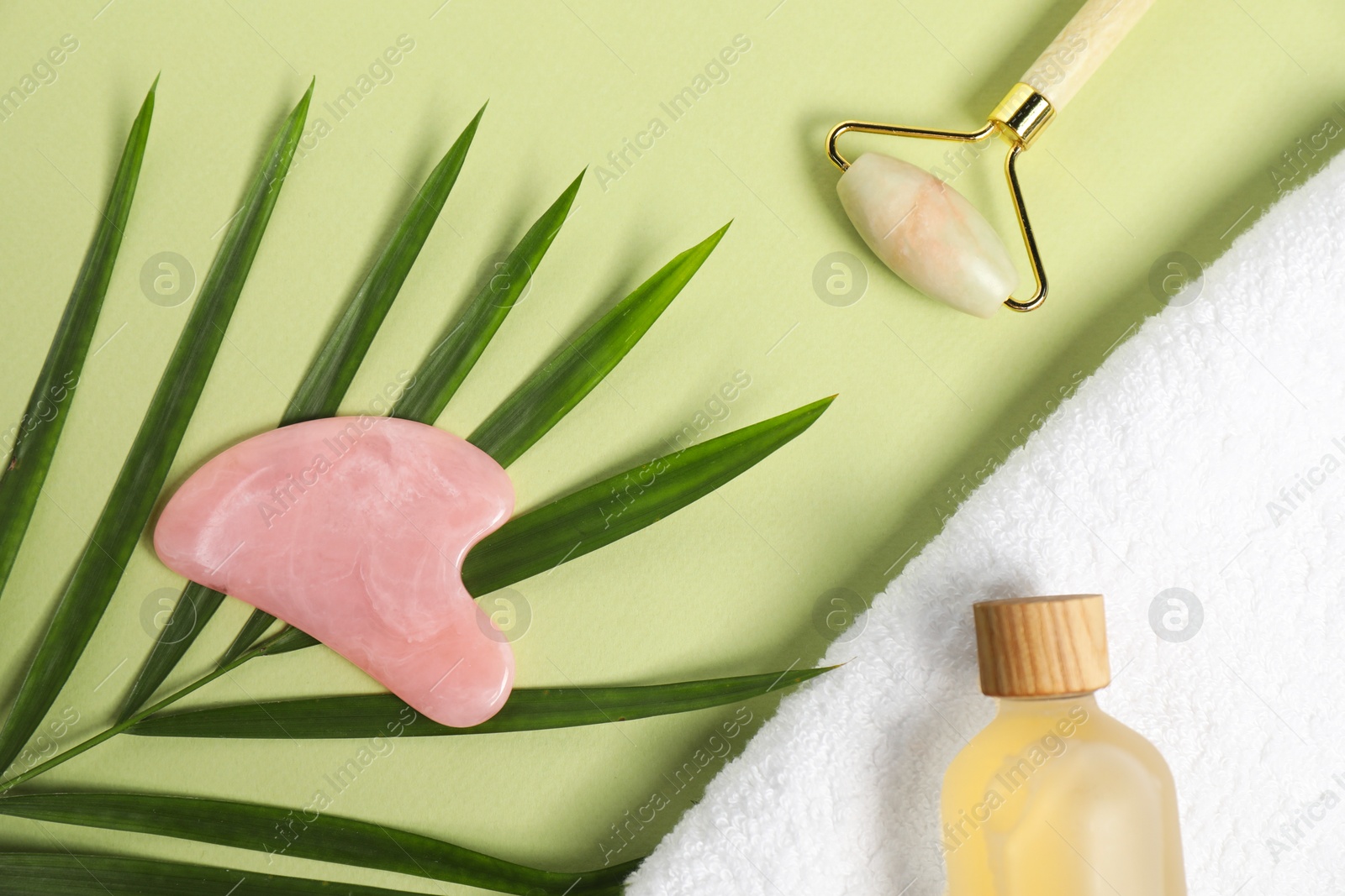 Photo of Face roller, gua sha tool, cosmetic product, towel and leaf on light green background, flat lay