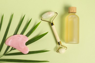 Photo of Face roller, gua sha tool, cosmetic product and leaf on light green background, flat lay