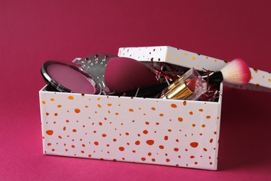 Photo of Christmas gift box with decorative cosmetics on dark pink background, closeup