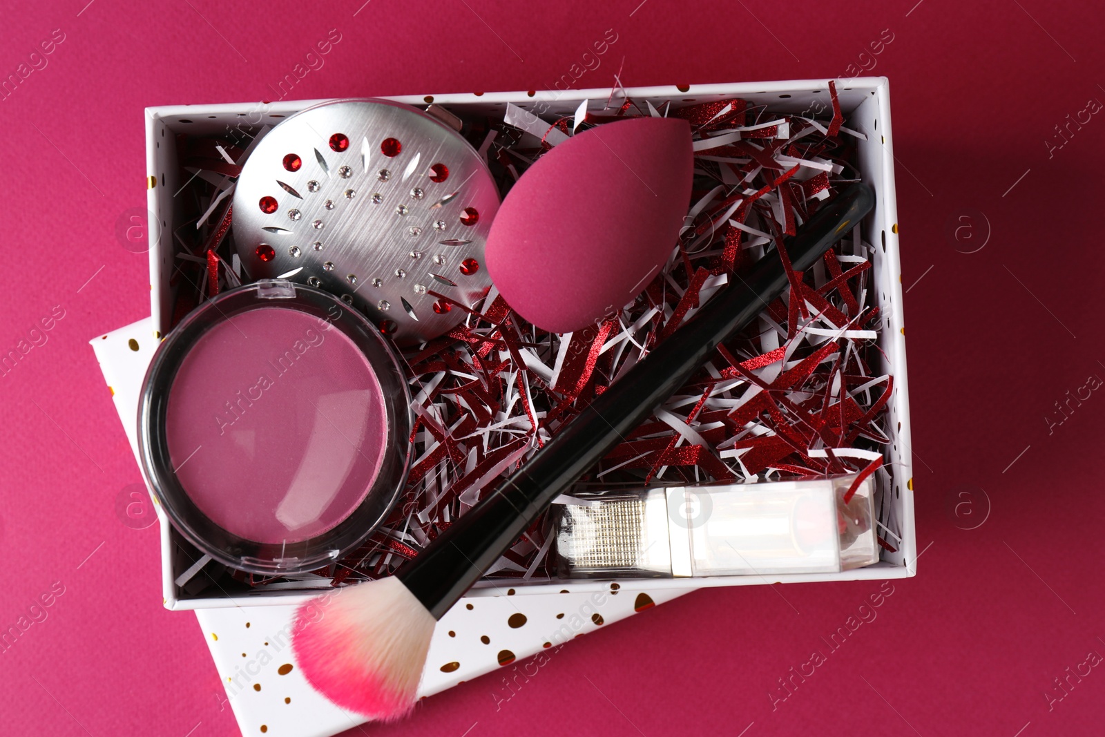 Photo of Christmas gift box with decorative cosmetics on dark pink background, top view