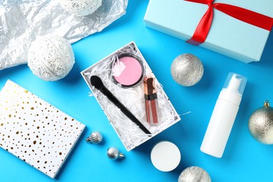 Photo of Decorative cosmetics as Christmas present. Makeup products, gift boxes and festive balls on light blue background, flat lay