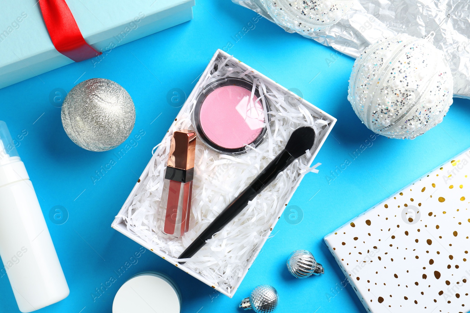 Photo of Decorative cosmetics as Christmas present. Makeup products, gift boxes and festive balls on light blue background, flat lay