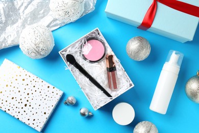 Photo of Decorative cosmetics as Christmas present. Makeup products, gift boxes and festive balls on light blue background, flat lay