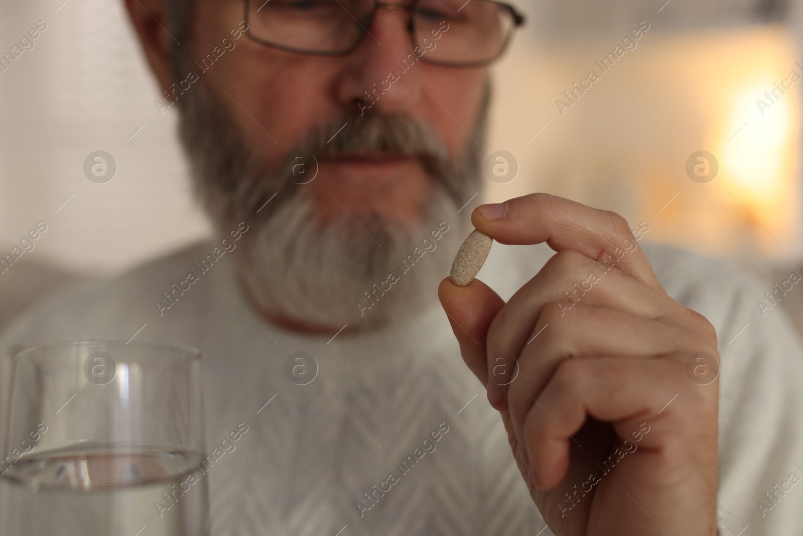 Photo of Senior man with pill and glass of water indoors, selective focus