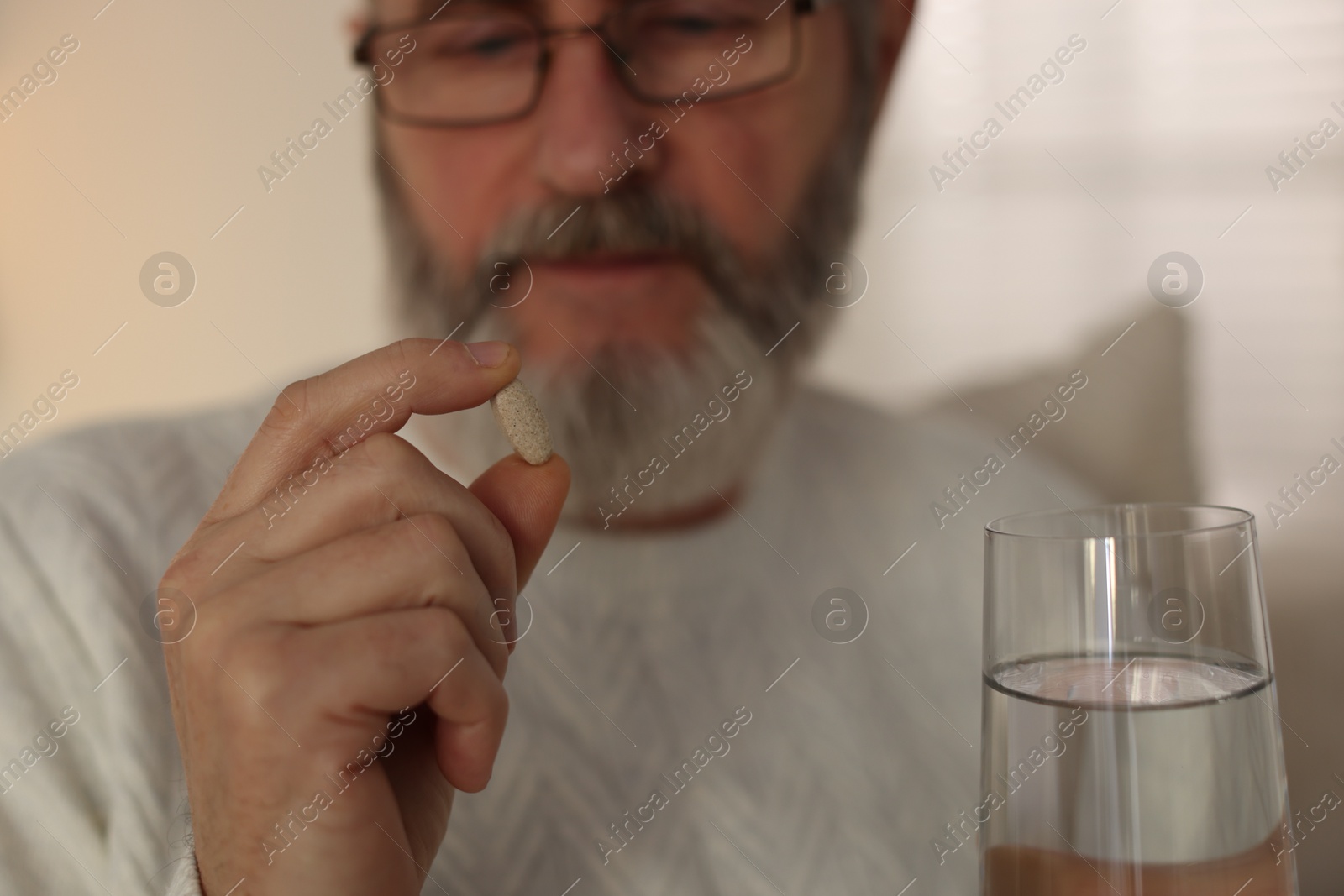 Photo of Senior man with pill and glass of water indoors, selective focus