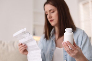 Photo of Woman with bottle of pills and instruction indoors, selective focus