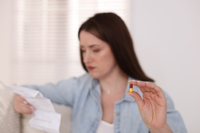 Photo of Woman with pill reading instruction indoors, selective focus