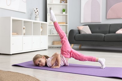 Photo of Little girl exercising on fitness mat at home. Sport activity