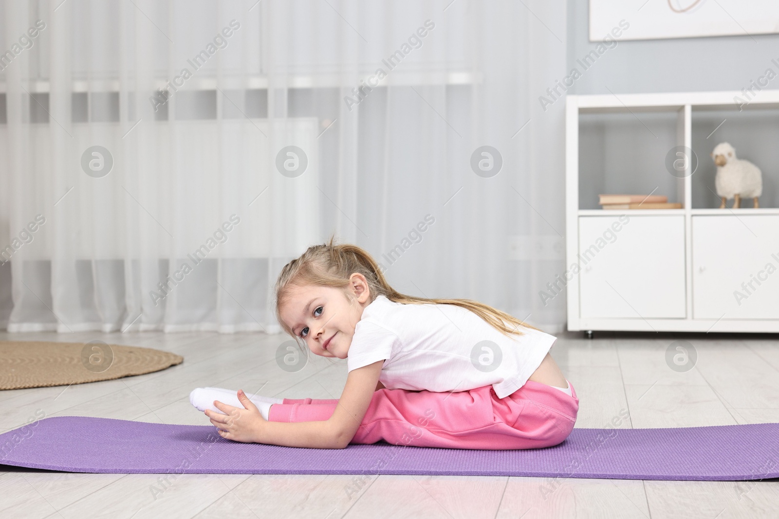 Photo of Little girl exercising on fitness mat at home. Sport activity