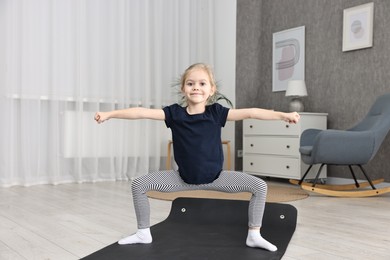 Photo of Little girl exercising on fitness mat at home. Sport activity